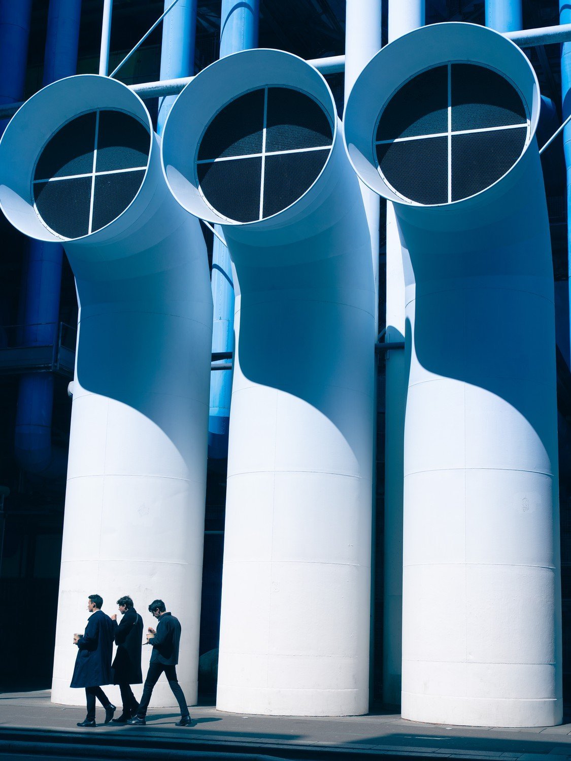 three men walking in front of large pipes