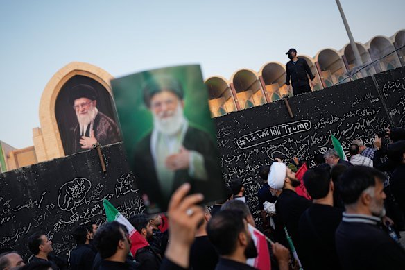 A mourner carries a portrait of Khamenei in front of a wall bearing the message “We will kill Trump” in Tehran. 