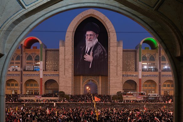 Mourners gather beneath a portrait of the late Iranian Supreme Leader Ayatollah Ali Khamenei during funeral ceremonies for Khamenei and members of his family.