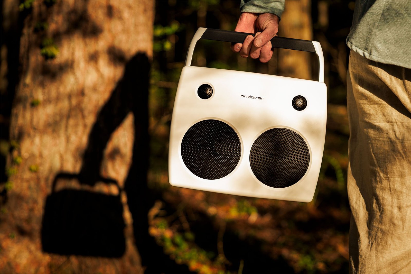 An Ivory Andover FreePlay speaker casts a shadow against a tree trunk