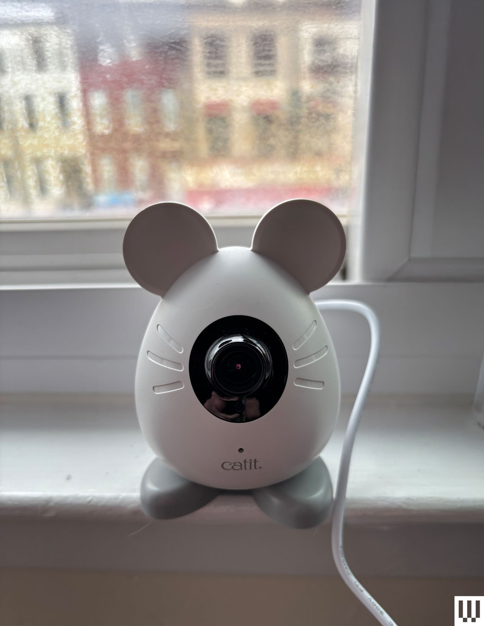 The white pet camera in the shape of a mouse sits on a white windowsill.