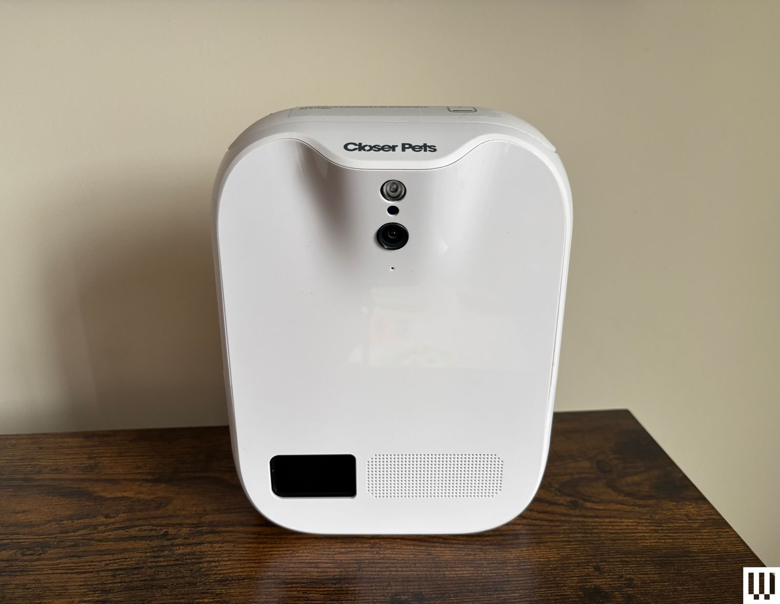 White rectangular treat dispensing pet chamber sits on a wooden shelf with cream wall background