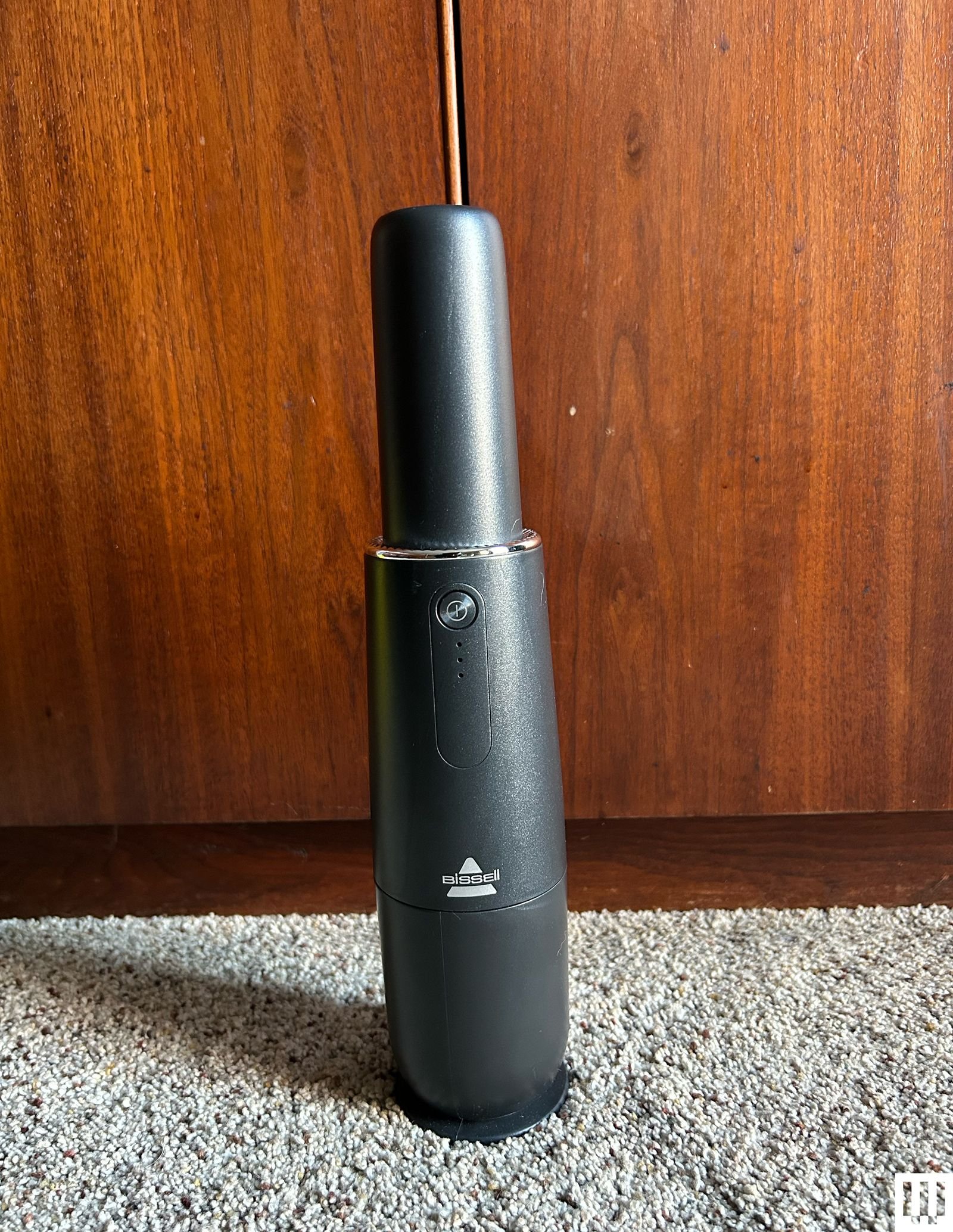 Bissell AeroSlim handheld vacuum leaning against a wooden panel with carpet underneath