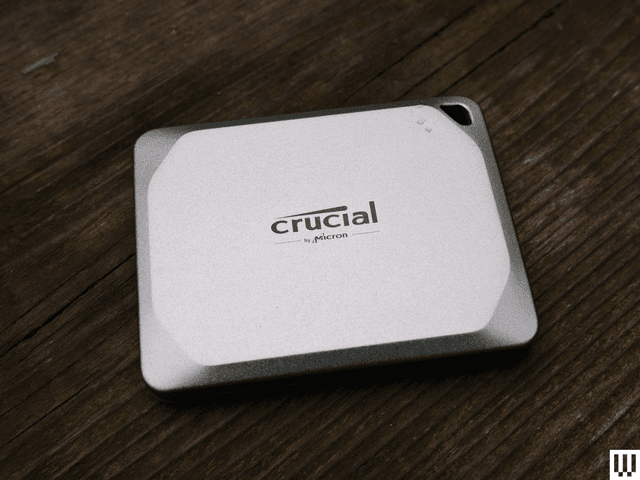 Crucial X9 square shaped silver external hard drive with angled corner edges on a dark wooden surface