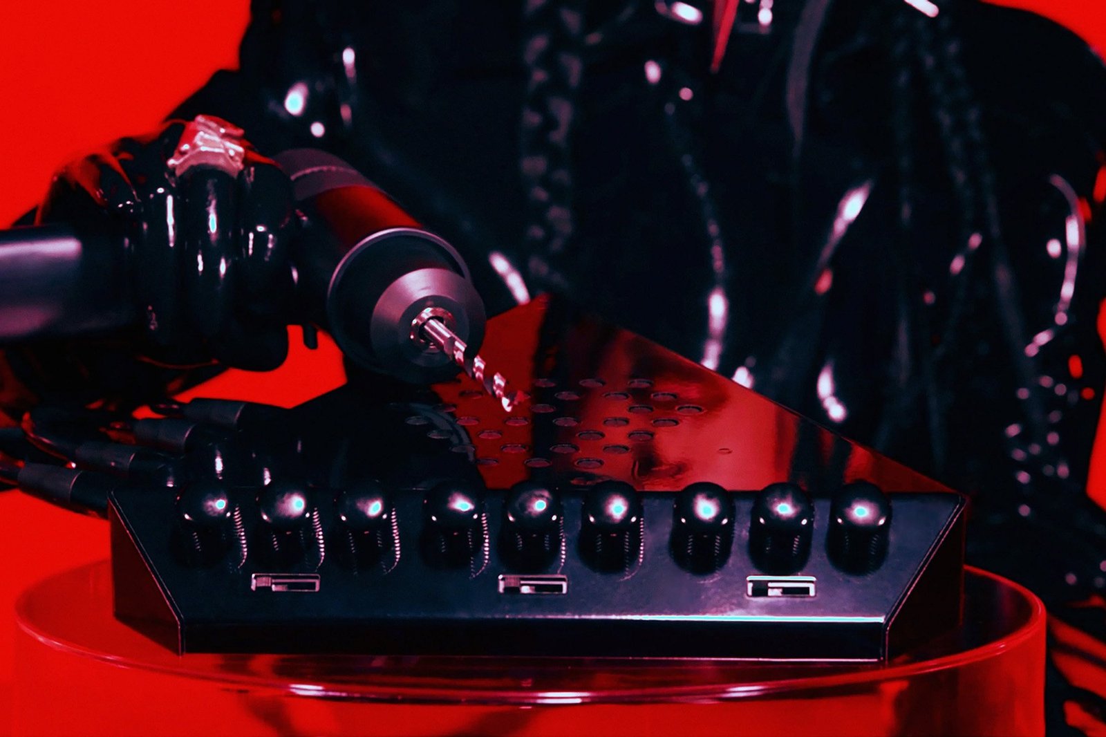 A close-up of the Eternal Research Demon Box's knobs and sliders with a devilish drill placed on top of it on a red background.