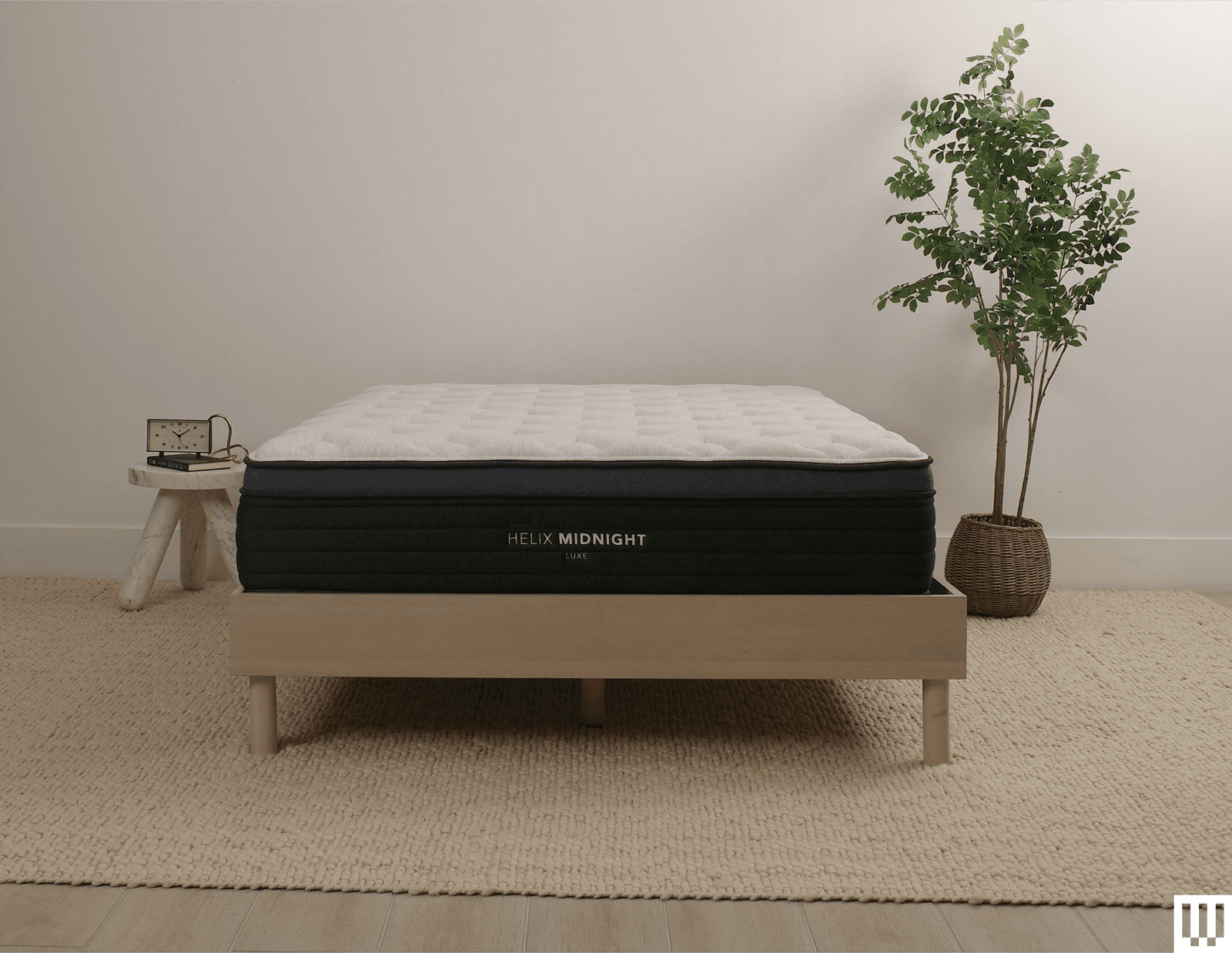 Helix Sleep Midnight Luxe a white mattress with blue piping on a minimalist wooden structure with nightstand and flowerpot...