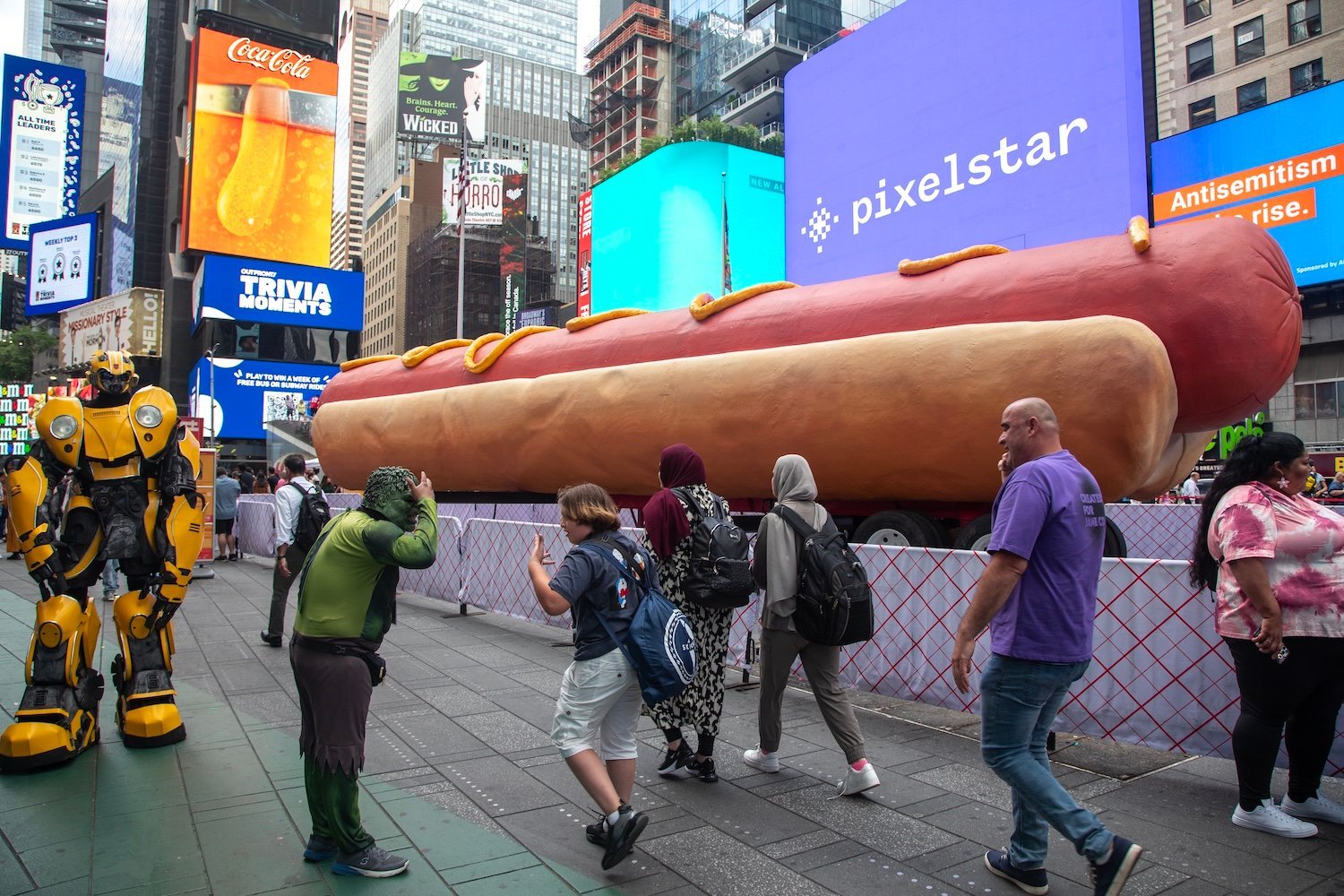 NEW YORK, NY - JUNE 12: People walk past a Hot Dog sculpture in Times Square on June 12, 2024 in New York City. At 65 feet long, Times Square's latest major public art installation, Hot Dog in the City, surpasses the record for the world's largest hot dog sculpture. (Photo by Liao Pan/China News Service/VCG via Getty Images)