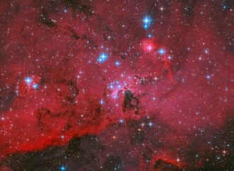 NASA’s Hubble captures a crimson cloud glowing with white and blue stars