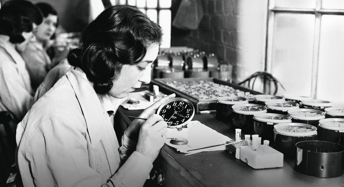 A woman in a historical photograph paints the face of a clock.