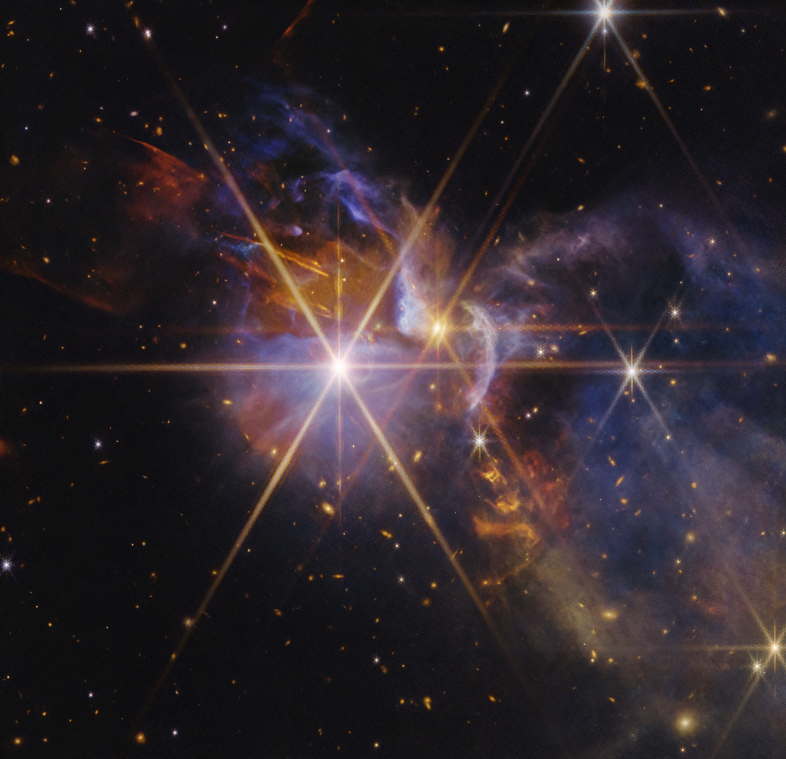 FS Tau, a star-forming nebula. Clouds of transparent blue and violet gas and dust extend from the center to the right. Several yellow and white protostars, some of which display Webb's eight-point diffraction pattern, are scattered throughout the clouds. Orange threads and filaments of gas extend from one of the protostars in the center to the upper left and lower right corners. There are numerous distant yellow and white galaxies scattered on the black background of space.