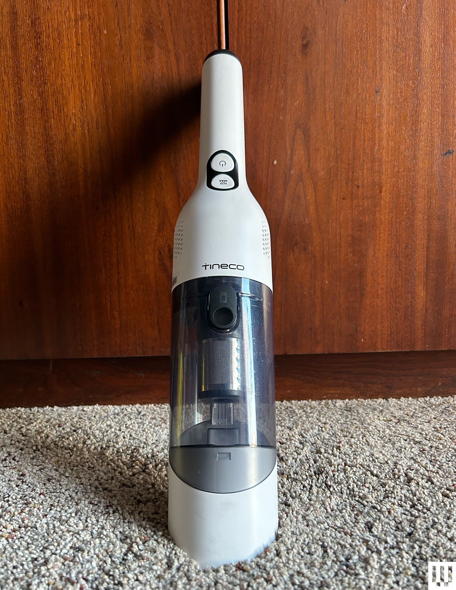 Tineco Go Mini cordless handheld vacuum cleaner leaning against a wooden panel and carpet