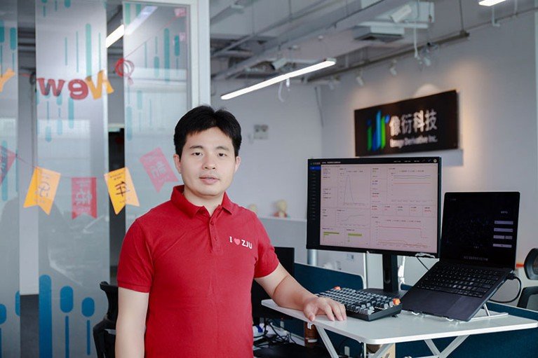 Cui Guangzhang stands at his computer at Hangzhou Xiangfan Technology. He wears a red t-shirt with the logo