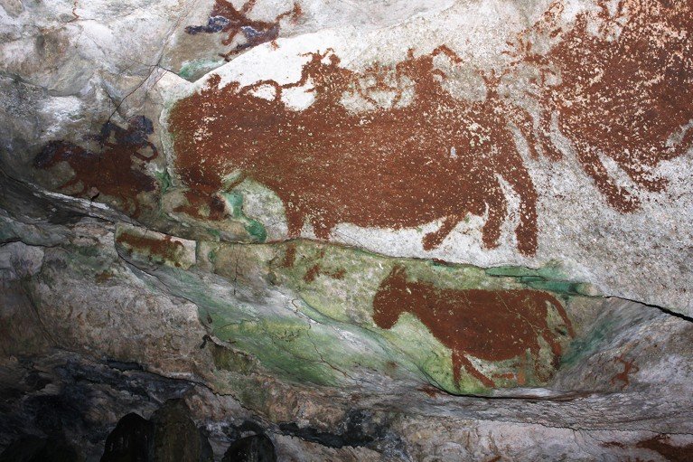 Reddish-brown drawings of human figures and four-legged animals adorn a green and gray rocky background.