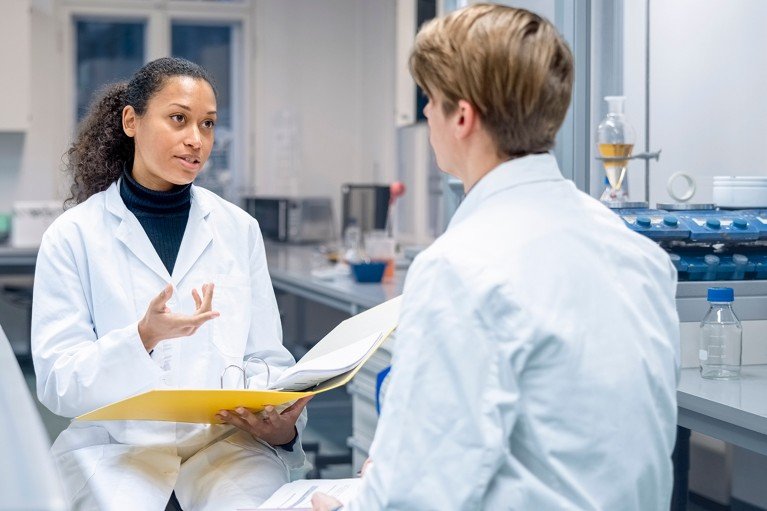 Female researcher holding a file and talking to a lab technician in a laboratory.