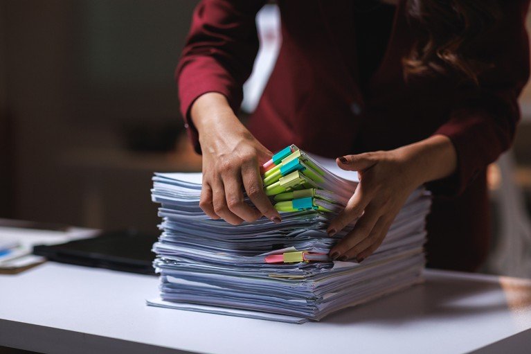 Woman organizing a large stack of office documents with colorful sticky notes and binder clips on a desk.