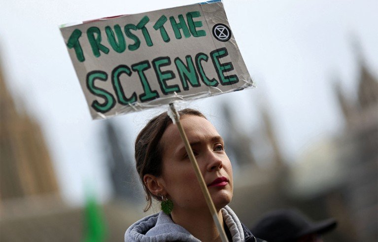 A protester holding a cardboard sign that said "TRUST THE SCIENCE"with the Extinction Rebellion logo.
