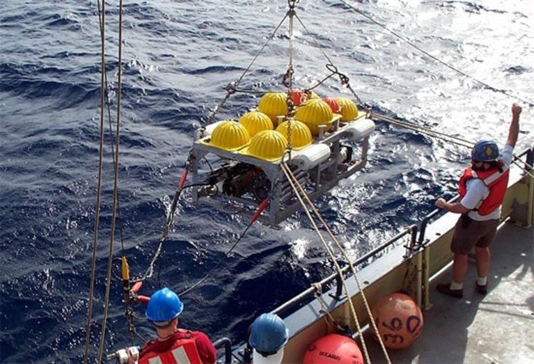 An ocean floor seismometer lowering from a ship into the water.