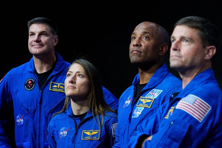 From left, Artemis II crew Jeremy Hansen, Christina Koch, Victor Glover and Reid Wiseman look on while standing against a black background.