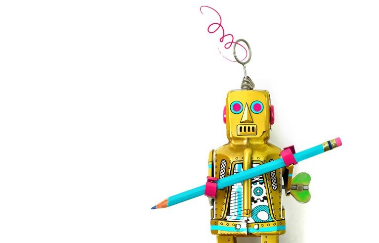Closeup of an old style toy robot on a white background holding a blue pencil.