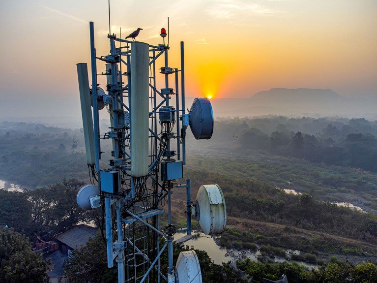 Telecommunications equipment and antenna mounted on a cell tower in a remote rural area with a backdrop of sunrise over the hills.