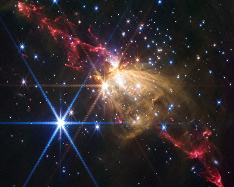 A star-forming region in space showing bright blue and yellow stars surrounded by bright red and orange gas clouds.