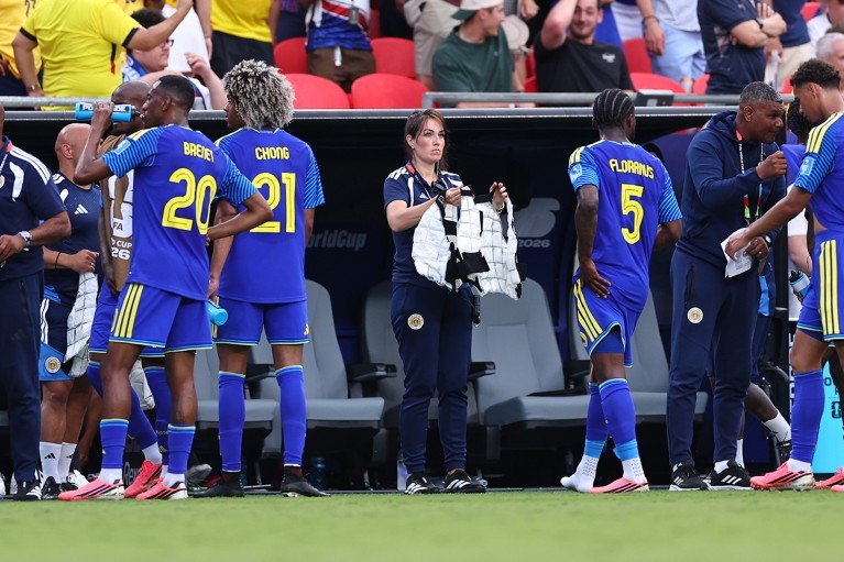 A woman holds out a white garment toward one of several men in blue soccer uniforms.