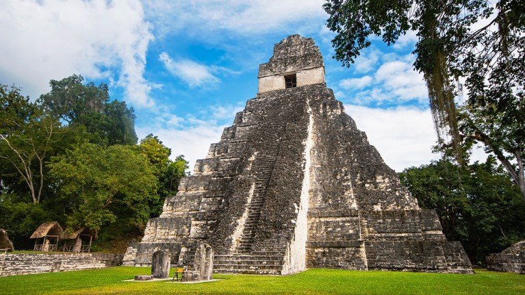 The well-preserved Temple of the Great Jaguar in Tikal, Guatemala. The shape is a distinctive pyramidal shape with a stepped design in a forest clearing.