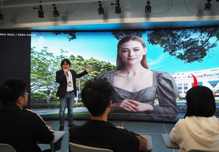 Pan Hui stands next to a digital teaching avatar on a large screen.