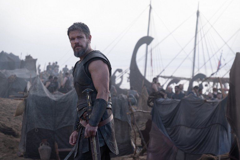 Still from the film The Odyssey, showing Matt Damon as Odysseus, on a beach with a ship in the background.