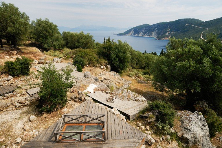 Elevated view of the School of Homer, archaeological site in Ithaca, Greece, showing stones among scrub vegetation near the coast.