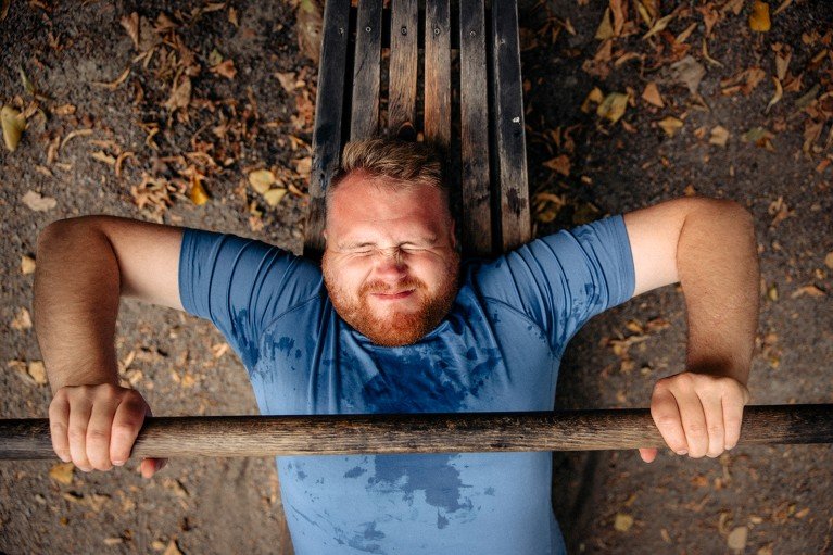 View from above of a man in full effort, doing bench press in an outdoor gym.