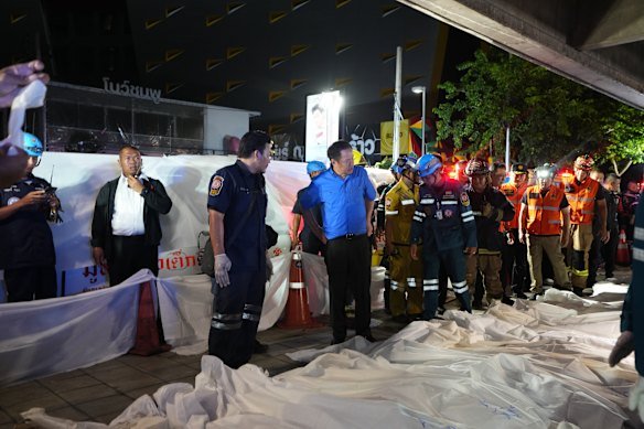 Thai Prime Minister Anutin Charnvirakul, in blue, at the scene of the fire, as the bodies of victims are placed in a row in Bangkok on Monday.