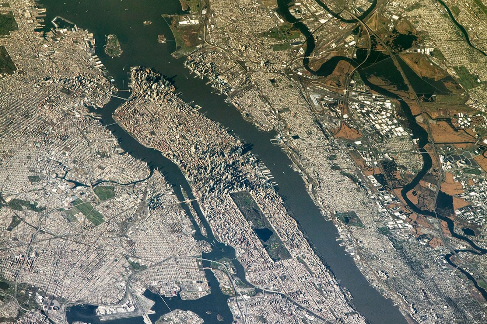 An aerial view shows New York New Jersey Stadium and the surrounding Meadowlands to the right, with the dense cityscape of Manhattan Island centered in the frame.