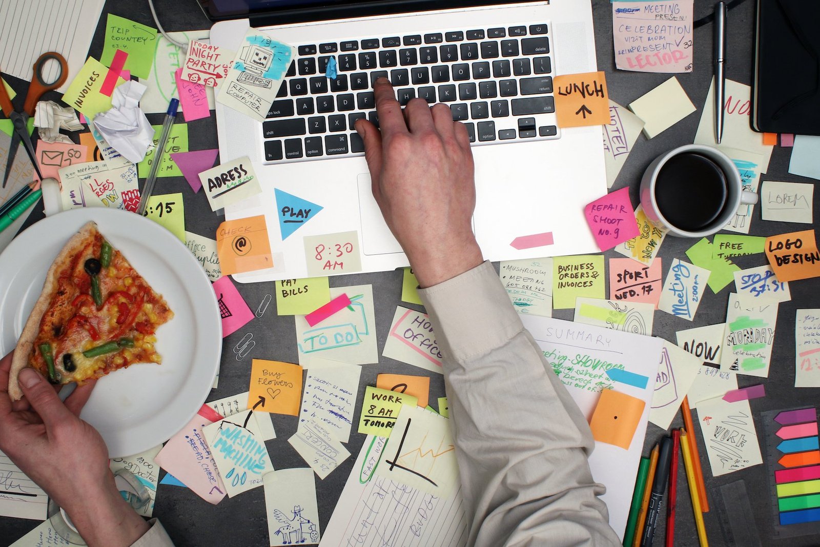 messy desk while someone works at their desk and eats pizza