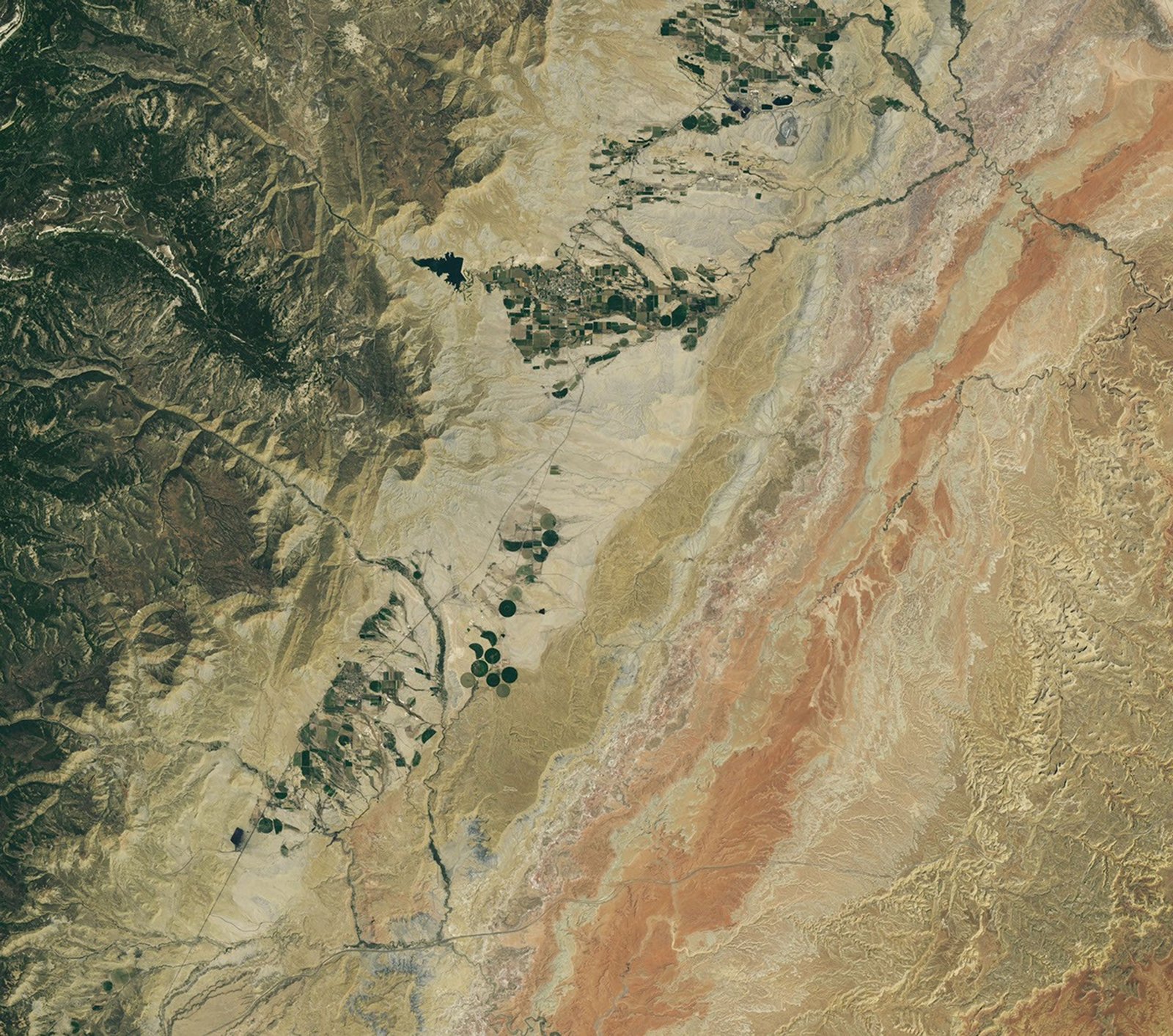 A dry tan valley containing some circular irrigated fields runs roughly north to south across the image.