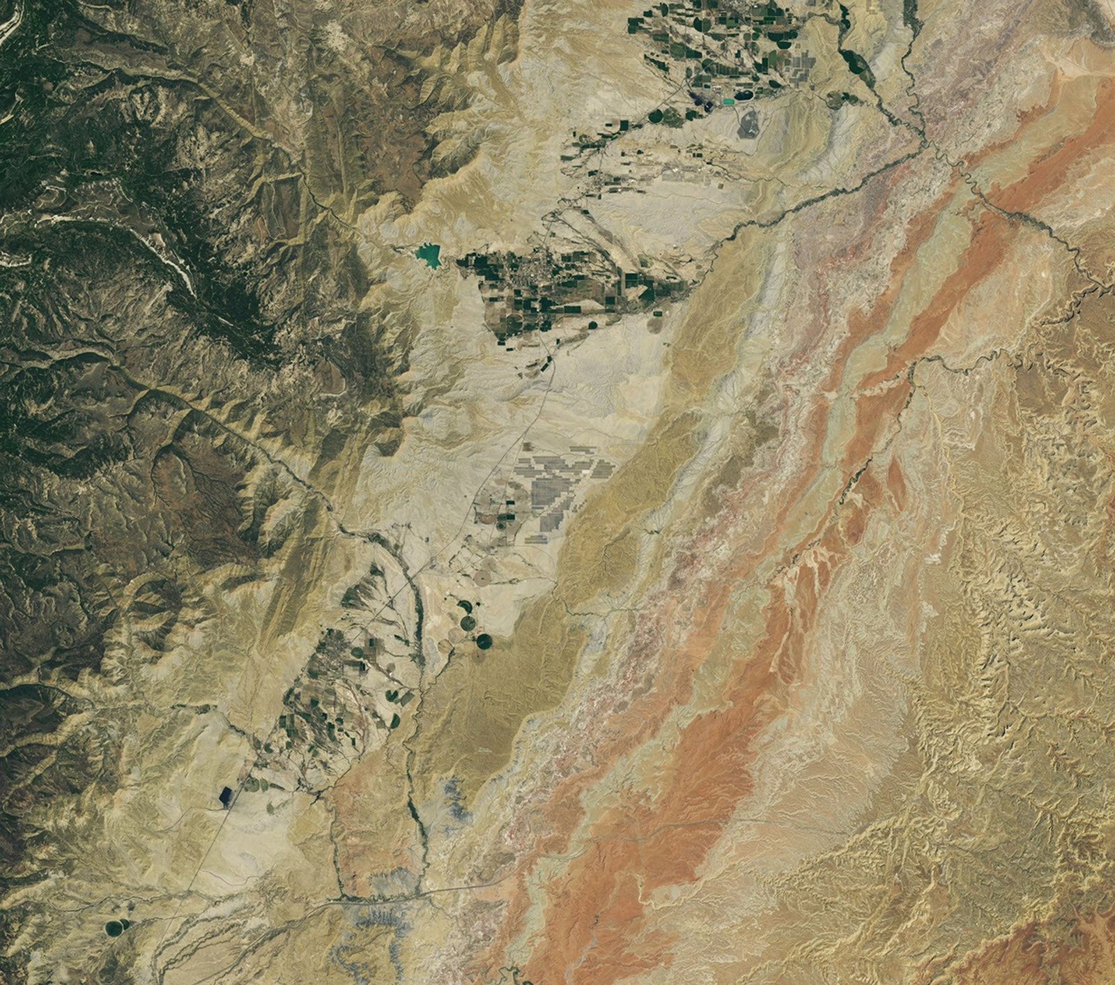 Grid-shaped arrays of solar panels cover parts of a valley floor in a brown, dry-looking area of ​​Utah.