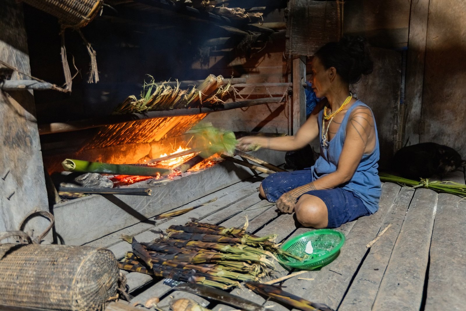 Mentawai woman cooking in the kitchen of traditional village house on Siberut island, West Sumatra, Indonesia. He dresses in blue and has tattoos.