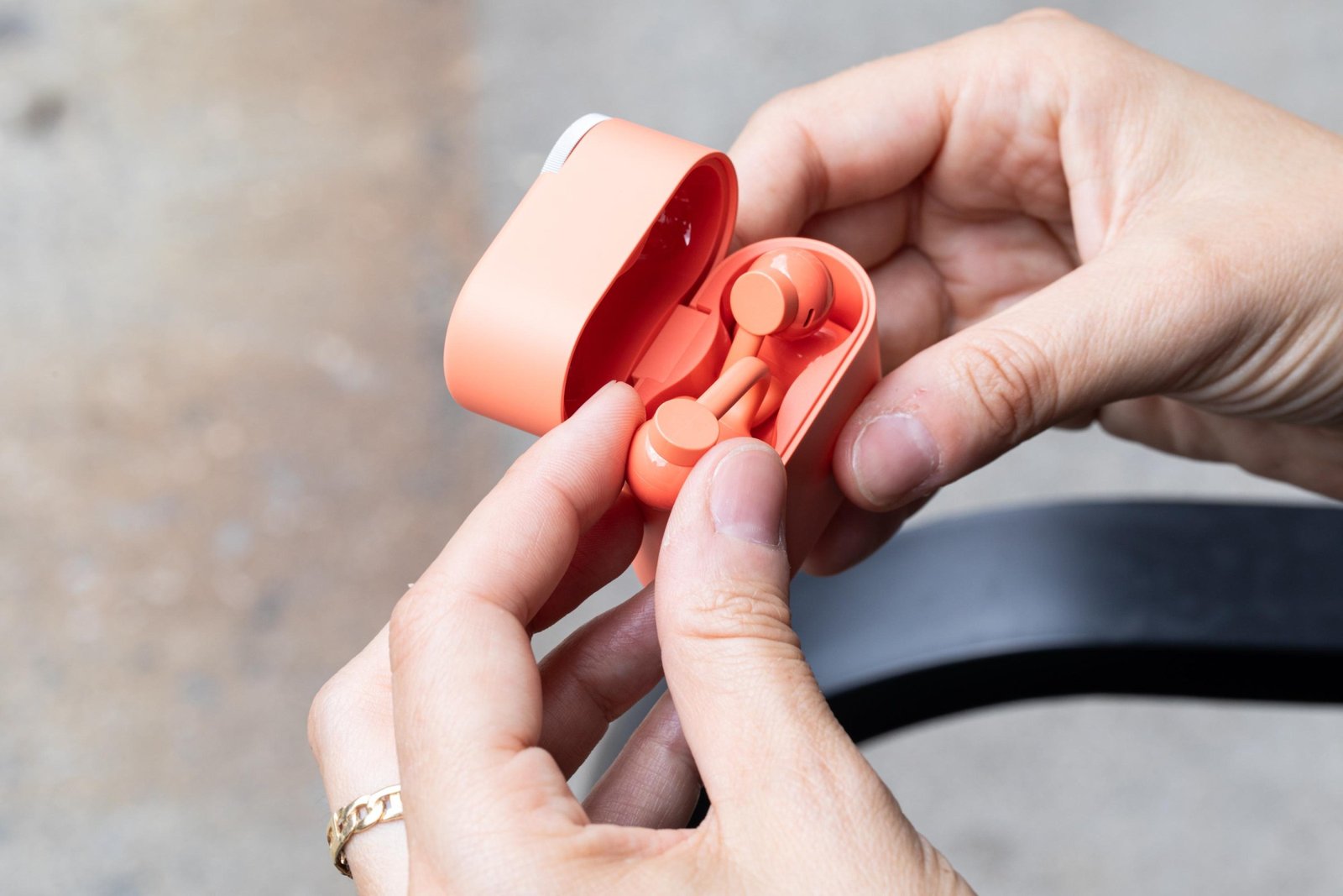 A hand holding the coral-colored CMF Clip Pro earbuds in their flip-top case.