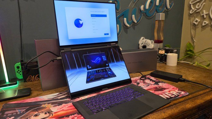 The front of the laptop showing the keyboard lit up and working, yet detached. The two screens are stacked vertically on top of one another, but the screens themselves are in horizonal orientation.