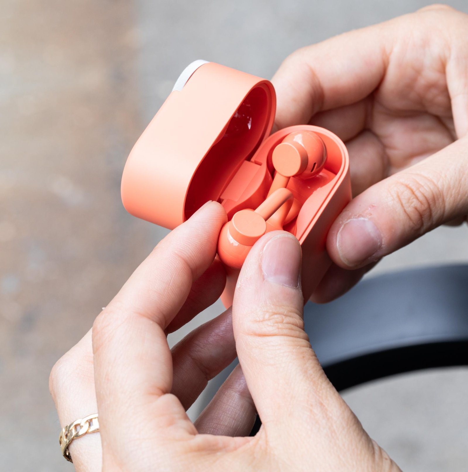 A hand holding the coral-colored CMF Clip Pro earbuds in their flip-top case.