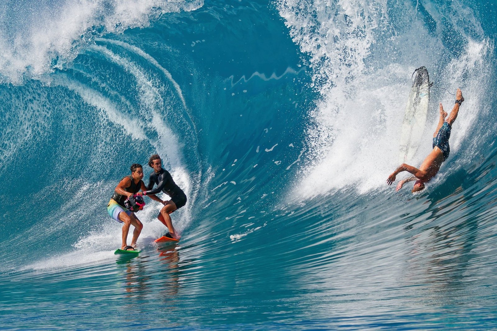 Three surfers converge on the same wave