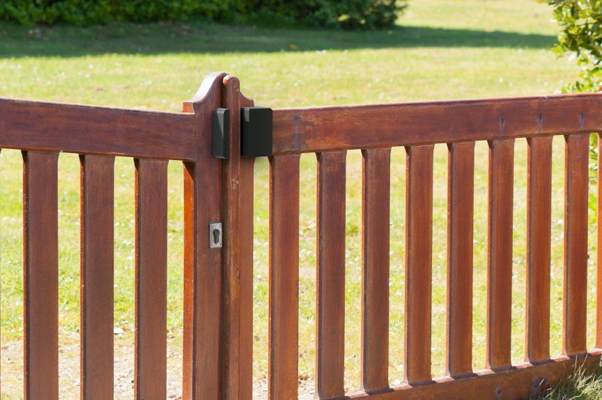 A black Abode sensor on a wood fence.