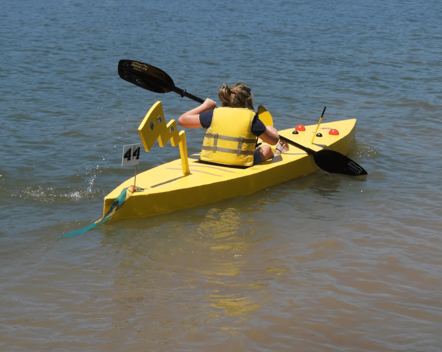 Woman paddling in cardboard kayak decorated like Pikachu from Pokemon