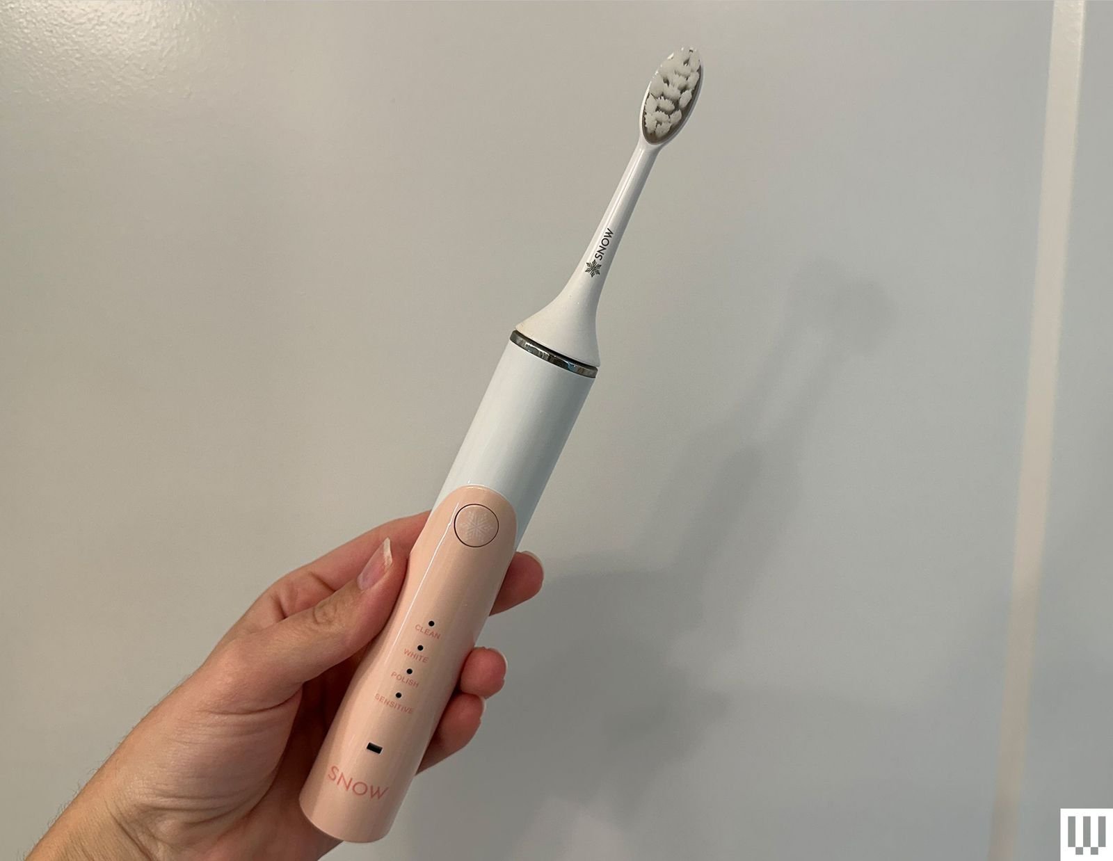 A hand holding up the Snow LED Whitening Electric Toothbrush in pink and white