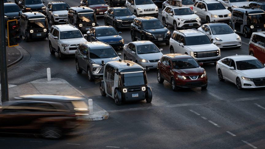 Three Zoox robotaxis wait in traffic among other cabs and private vehicles.