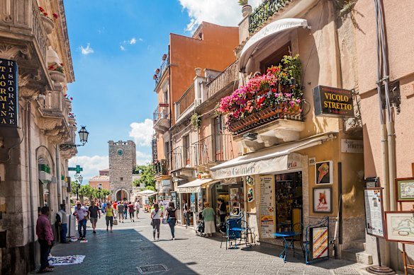 Visitors stroll through the pedestrianised main street of Taormina near to its city gate.