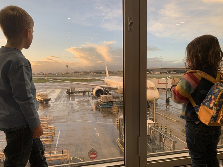 A boy and a girl look out of the window at a plane on the tarmac at Heathrow Airport.