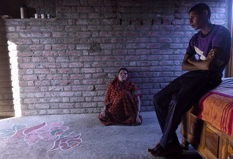 Two family members of a deceased cotton farmer sit quietly in a brick house, their expressions conveying mourning and sorrow.