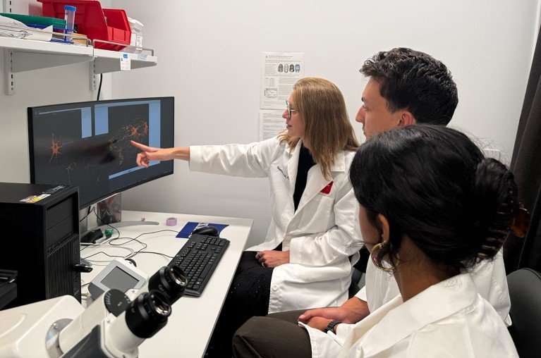 Valentina Fossati mentoring team members seated around a computer in a laboratory.