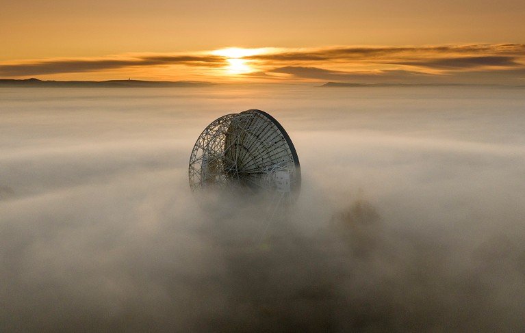 Aerial view the Lovell Telescope at Jodrell Bank emerging above morning fog at sunrise.